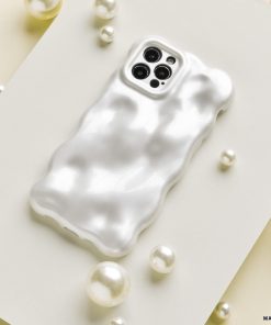 An iPhone with a glossy, ripple-patterned white case is displayed on a white rectangular surface. Surrounding the phone are scattered white pearls and Coconut Lane's 3D Pearl Phone Case - White, adding a touch of elegance to the composition.