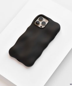 A black iPhone with a Coconut Lane 3D Boujee Phone Case in Matte Black rests on a white surface. The phone's camera array is visible on the back, featuring three lenses and a flash. The matte black finish of the extra protective, minimalist design emphasizes the soft, wavy texture and shape of the case.