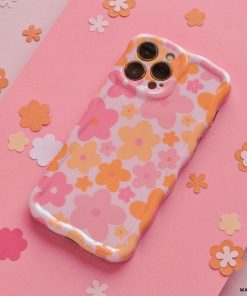 A Coconut Lane Wavy Phone Case - Pink & Orange Bloom lies on a pink surface scattered with small, flower-shaped cutouts in various shades of pink and orange. The case's extra protective design complements the cohesive, vibrant, and playful floral aesthetic.