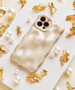 Displayed on a flat surface, surrounded by decorative gold foil fragments and scattered pearl beads, is the textured, glossy beige 3D Pearl Phone Case - Gold from Coconut Lane. This stylish and luxurious case features a wavy design and has precise cutouts for the camera lenses.
