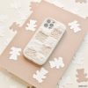 A Cosy Teddy Phone Case in Vanilla Biscuit by Coconut Lane is placed on a beige sheet of paper. Surrounding the phone are small, white bear-shaped cutouts scattered on a cream-colored surface, creating a cozy and whimsical scene.