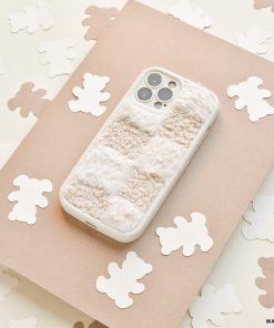A Cosy Teddy Phone Case in Vanilla Biscuit by Coconut Lane is placed on a beige sheet of paper. Surrounding the phone are small, white bear-shaped cutouts scattered on a cream-colored surface, creating a cozy and whimsical scene.