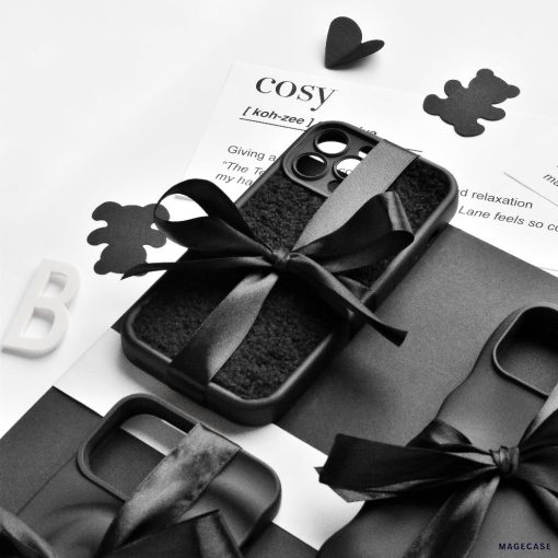 A monochrome image featuring the Cosy Teddy Phone Case - Black by Coconut Lane, tied with a black ribbon and placed on a black-and-white textured surface. Also shown are a dictionary definition of "cosy," black teddy bear cutouts, and the letter "B.