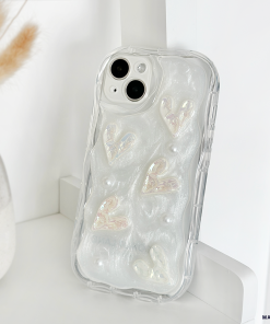 The Pearly Hearts Phone Case - Clear by Coconut Lane is an iridescent phone case with a textured design featuring raised, shimmering hearts and small pearl-like embellishments. This extra protective case is propped up on a white surface next to a vase containing dried wheat stalks.