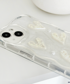A smartphone with a dual-camera setup is placed on a white surface. The phone is encased in Coconut Lane's Pearly Hearts Phone Case - Clear, featuring a pearly, wavy texture and raised designs of hearts. The image focuses on the back of the phone, highlighting the camera and the details of the Pearly Hearts Phone Case - Clear.