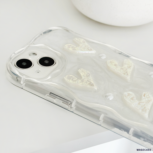 A smartphone with a dual-camera setup is placed on a white surface. The phone is encased in Coconut Lane's Pearly Hearts Phone Case - Clear, featuring a pearly, wavy texture and raised designs of hearts. The image focuses on the back of the phone, highlighting the camera and the details of the Pearly Hearts Phone Case - Clear.