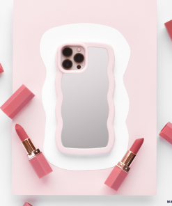 A smartphone featuring the Curvy Mirror Phone Case in Pink by Coconut Lane is centered on a white and pink abstract background. Around the phone, several pink lipsticks, each with a rose gold base and cap, are symmetrically arranged.