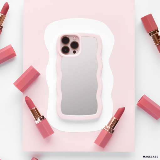 A smartphone featuring the Curvy Mirror Phone Case in Pink by Coconut Lane is centered on a white and pink abstract background. Around the phone, several pink lipsticks, each with a rose gold base and cap, are symmetrically arranged.