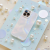 An iridescent iPhone with a Coconut Lane Mother of Pearl Phone Case is displayed on a light blue sparkly board. The background is adorned with various sizes of pearls and holographic circles, creating a whimsical and elegant arrangement.