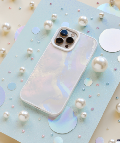 An iridescent iPhone with a Coconut Lane Mother of Pearl Phone Case is displayed on a light blue sparkly board. The background is adorned with various sizes of pearls and holographic circles, creating a whimsical and elegant arrangement.