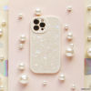 The Moonstone Pearl Phone Case by Coconut Lane adorns a white smartphone with an iridescent shell, which is laid on a pink, textured surface. Surrounding the phone are various-sized pearl-like beads, creating a refined and elegant arrangement. The phone's camera lenses are prominently displayed in the top left corner.