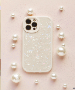 The Moonstone Pearl Phone Case by Coconut Lane adorns a white smartphone with an iridescent shell, which is laid on a pink, textured surface. Surrounding the phone are various-sized pearl-like beads, creating a refined and elegant arrangement. The phone's camera lenses are prominently displayed in the top left corner.