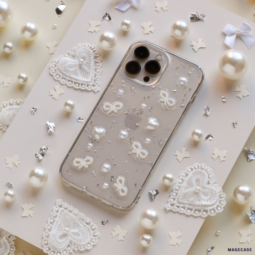 The Coquette Dreams Phone Case by Coconut Lane, crafted as an ultra-protective iPhone 15 case, features a clear base adorned with white lace patterns, pearls, and glitter. It is displayed on a decorated surface that includes scattered white lace hearts, tiny pearls, metallic star-shaped confetti, and small white bows.