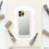 A sleek and stylish iPhone adorned with the Coconut Lane Curvy Mirror Phone Case in Cream is centered on a piece of off-white paper. The phone's camera is visible, reflecting off the back of the case. Surrounding the device are six muted beige lipsticks, some with their caps removed, arranged in a circular pattern.