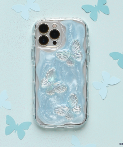 A smartphone encased in the Shimmer Blue Butterflies Phone Case by Coconut Lane, which is clear and extra protective with a wavy texture resembling flowing water, lies on a light blue background adorned with scattered paper butterfly cutouts. The phone has a triple-lens camera system.
