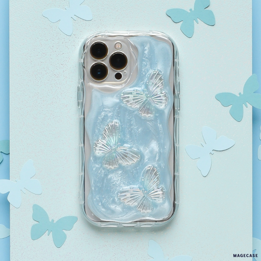 A smartphone encased in the Shimmer Blue Butterflies Phone Case by Coconut Lane, which is clear and extra protective with a wavy texture resembling flowing water, lies on a light blue background adorned with scattered paper butterfly cutouts. The phone has a triple-lens camera system.