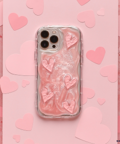 A Coconut Lane Shimmer Pink Hearts Phone Case, snugly fitting a smartphone, lies on a pink, textured background. Additional paper hearts in various shades of pink are scattered around the phone, creating a romantic, heart-themed scene.