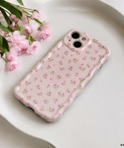 A pink smartphone with a Coconut Lane Wavy Phone Case - Ditsy Floral Pink, featuring small pink and green patterns, lies on a white tray. A bouquet of pink flowers rests beside the phone, adding a touch of elegance to the composition.