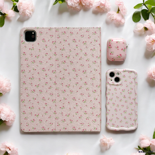 A tablet, a phone protected by Coconut Lane's Wavy Phone Case in Ditsy Floral Pink, and an AirPods case all featuring matching pink floral designs are arranged on a white surface surrounded by pale pink blossoms. The cases showcase a delicate pattern of ditsy floral pink flowers, creating a cohesive and aesthetically pleasing look.