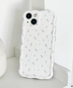 The image features a white smartphone encased in a Wavy Phone Case - Ditsy Floral White by Coconut Lane, offering extra protection and a decorative touch with its subtle floral pattern. The phone, equipped with dual cameras, is leaning against a white textured object on a smooth white surface.