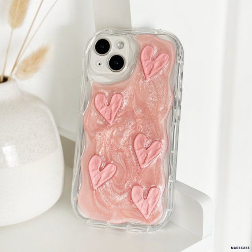 A Coconut Lane Shimmer Pink Hearts Phone Case featuring an extra protective clear design with pink swirls and five raised shimmer pink hearts is propped up against a white vase with dried wheat stalks. The background is a clean, white surface.