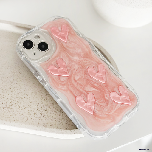 A smartphone encased in Coconut Lane's Shimmer Pink Hearts Phone Case, an extra protective transparent cover showcasing a pink and white marbled design adorned with six raised shimmer pink hearts. The phone is set on a light-colored speckled surface, creating a clean and minimalist aesthetic.